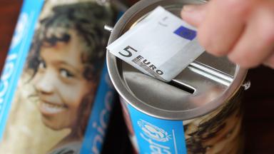 Eine Hand wirft einen Fünfeuroschein in eine Dose auf der Unicef steht