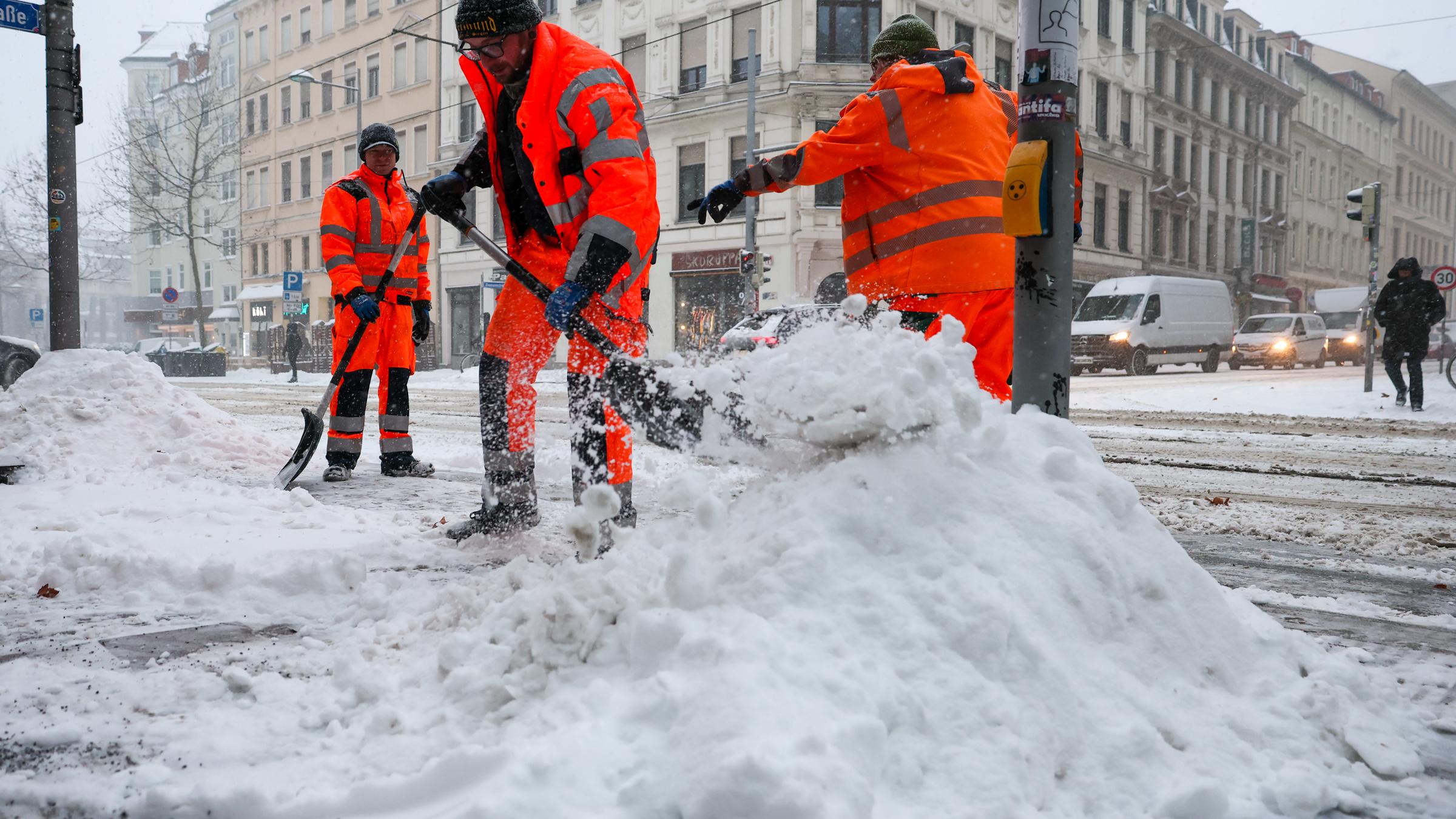 Mitarbeiter der Stadtreinigung räumen Schnee an einer Kreuzung. 