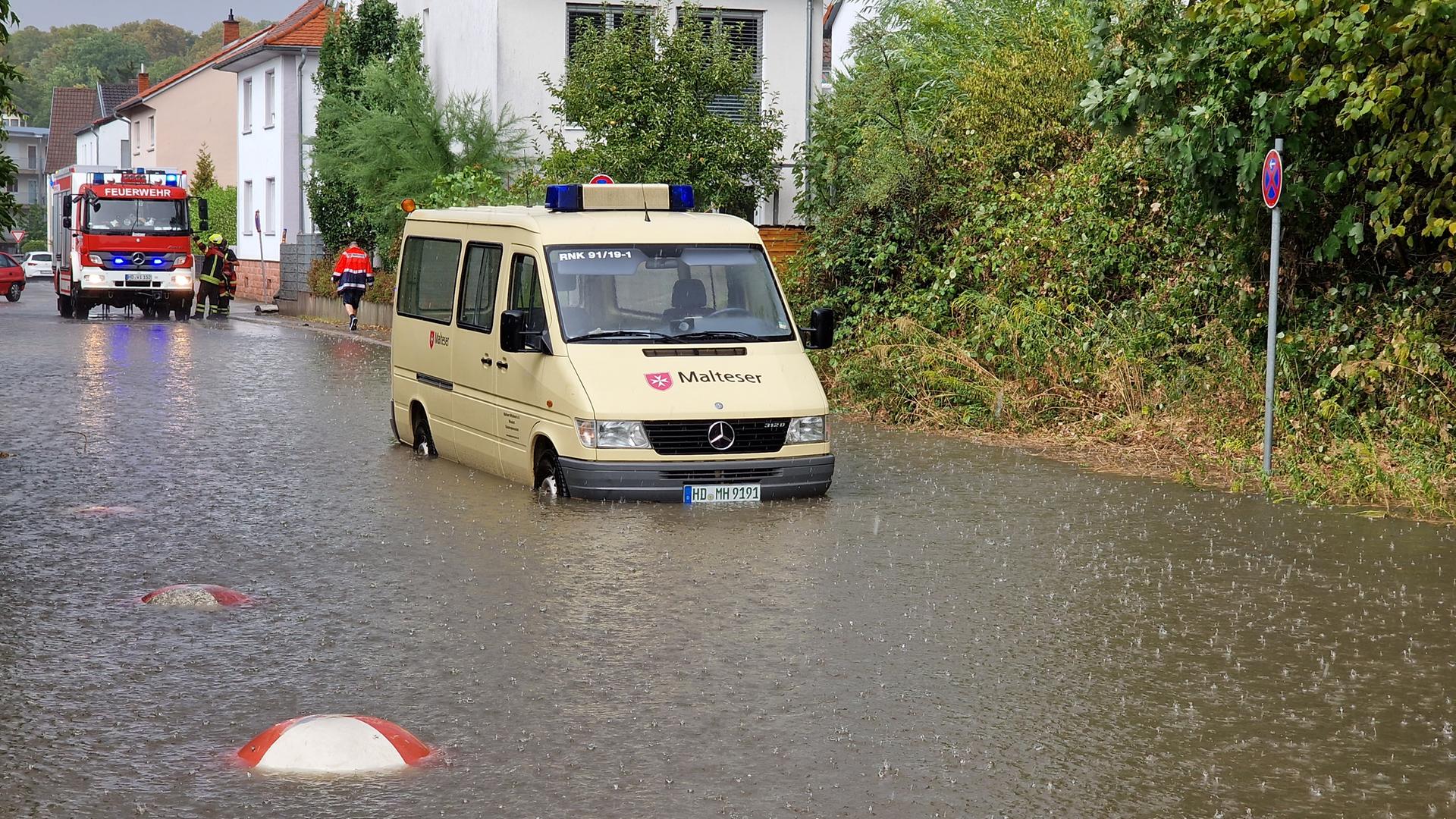Eine überflutete Straße. Zwei Einsatzfahrzeuge stehen vor einem Haus.