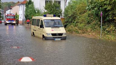 Eine überflutete Straße. Zwei Einsatzfahrzeuge stehen vor einem Haus.