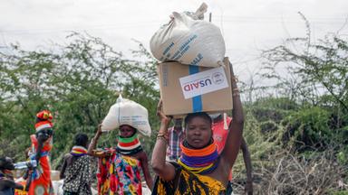 Frauen tragen Säcke mit Essen von USAID in Kenia.
