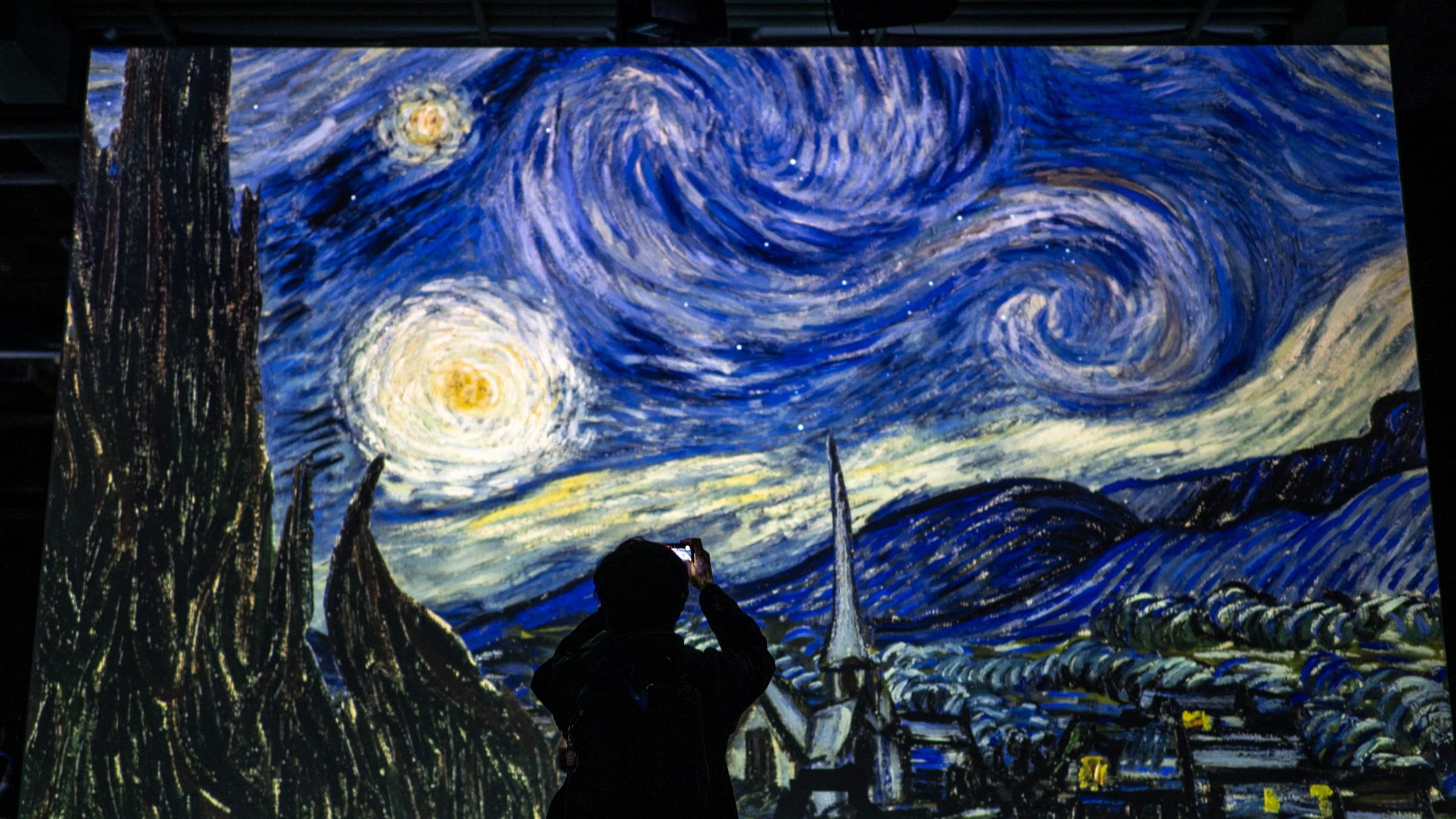 Silouette von Mann steht vor digitaler, übergroßer Version von Vincent van Gogh's Gemälde "Sternennacht" und macht ein Video in einer Ausstellung in Japan.