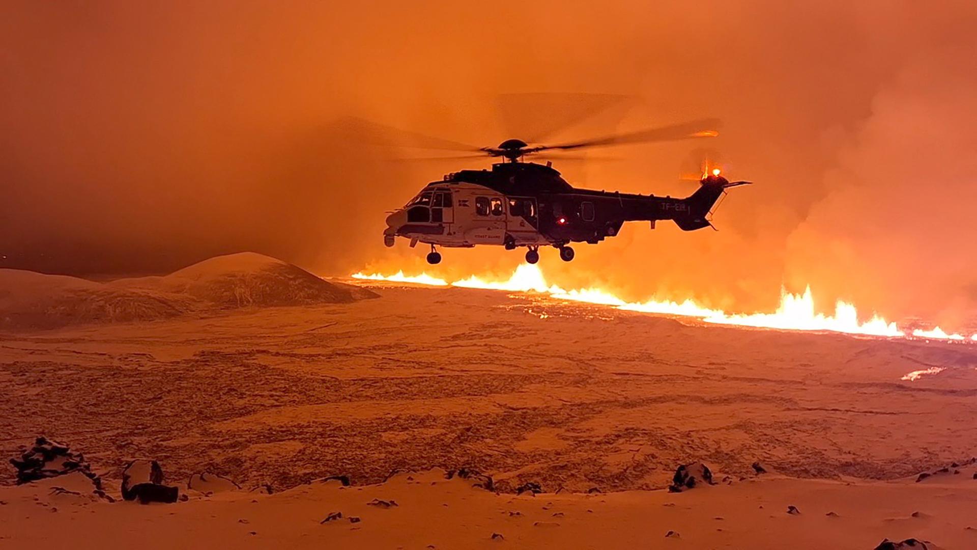 Hubschrauber vor Feuer- und Aschelandschaft nach Vulkanausbruch.