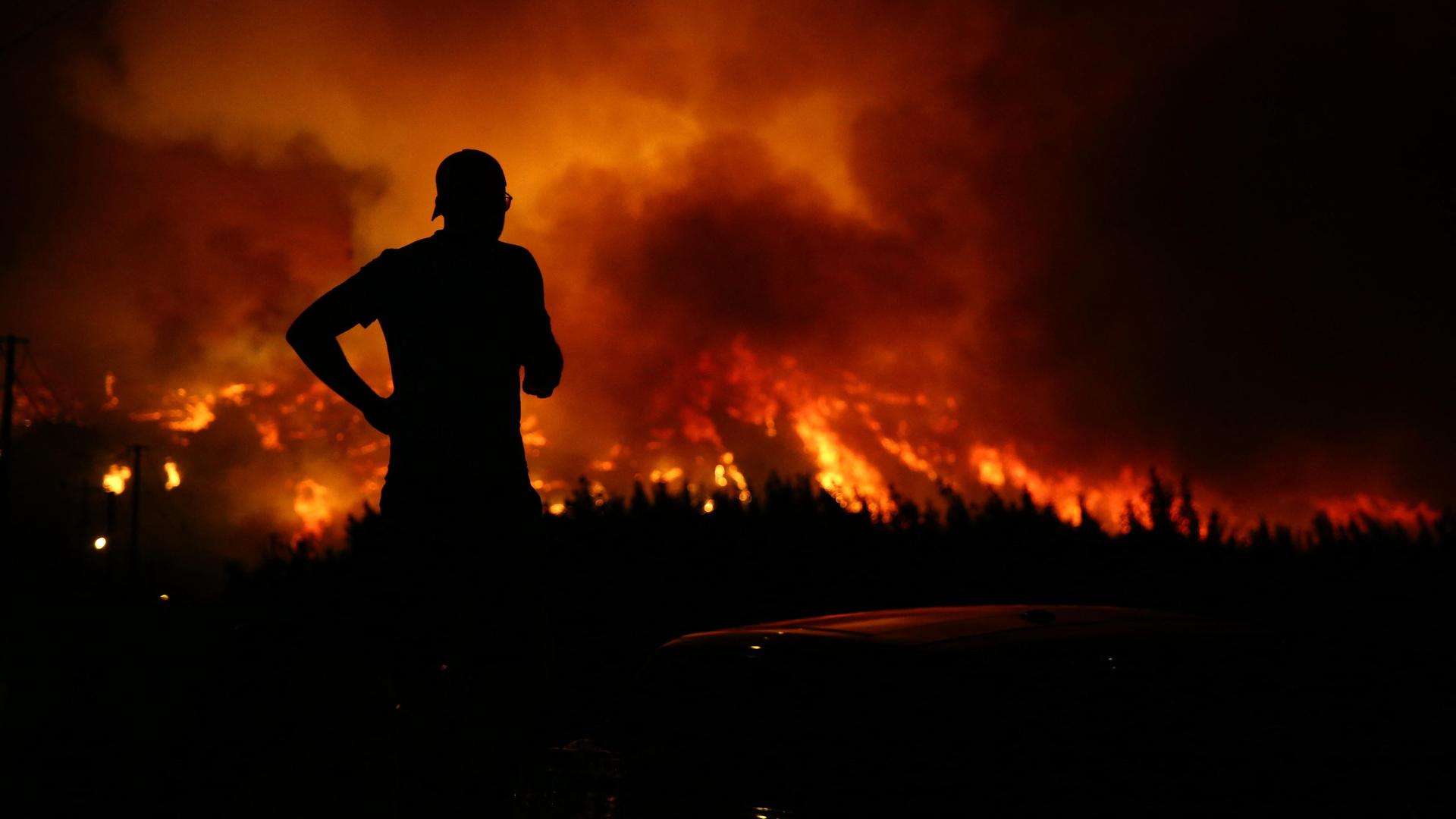 Ein Mann steht vor einem brennenden Wald bei Nacht