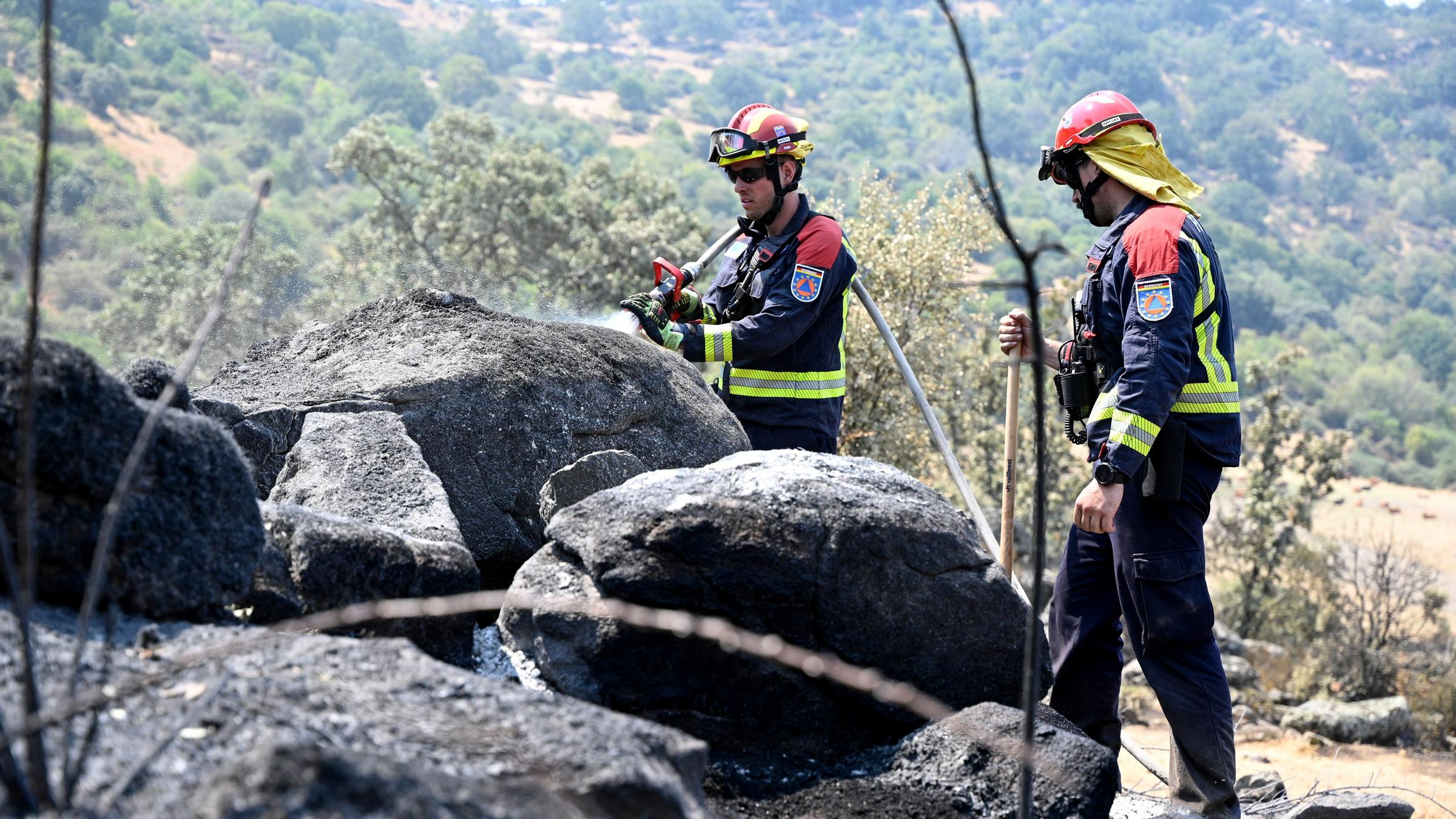 Deutsche Feuerwehrleute spritzen in der Region Extremadura Wasser auf einen bereits abgebrannten Bereich, suchen nach möglichen Glutnestern.