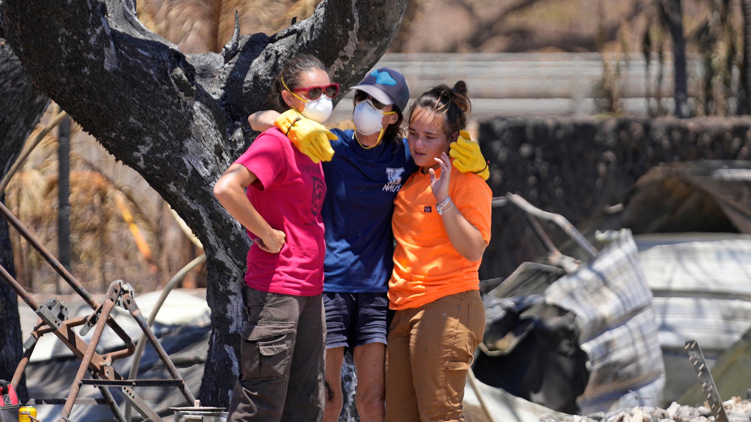 Frauen umarmen sich, nachdem sie sich durch die Trümmer eines von einem Waldbrand zerstörten Hauses gegraben haben,