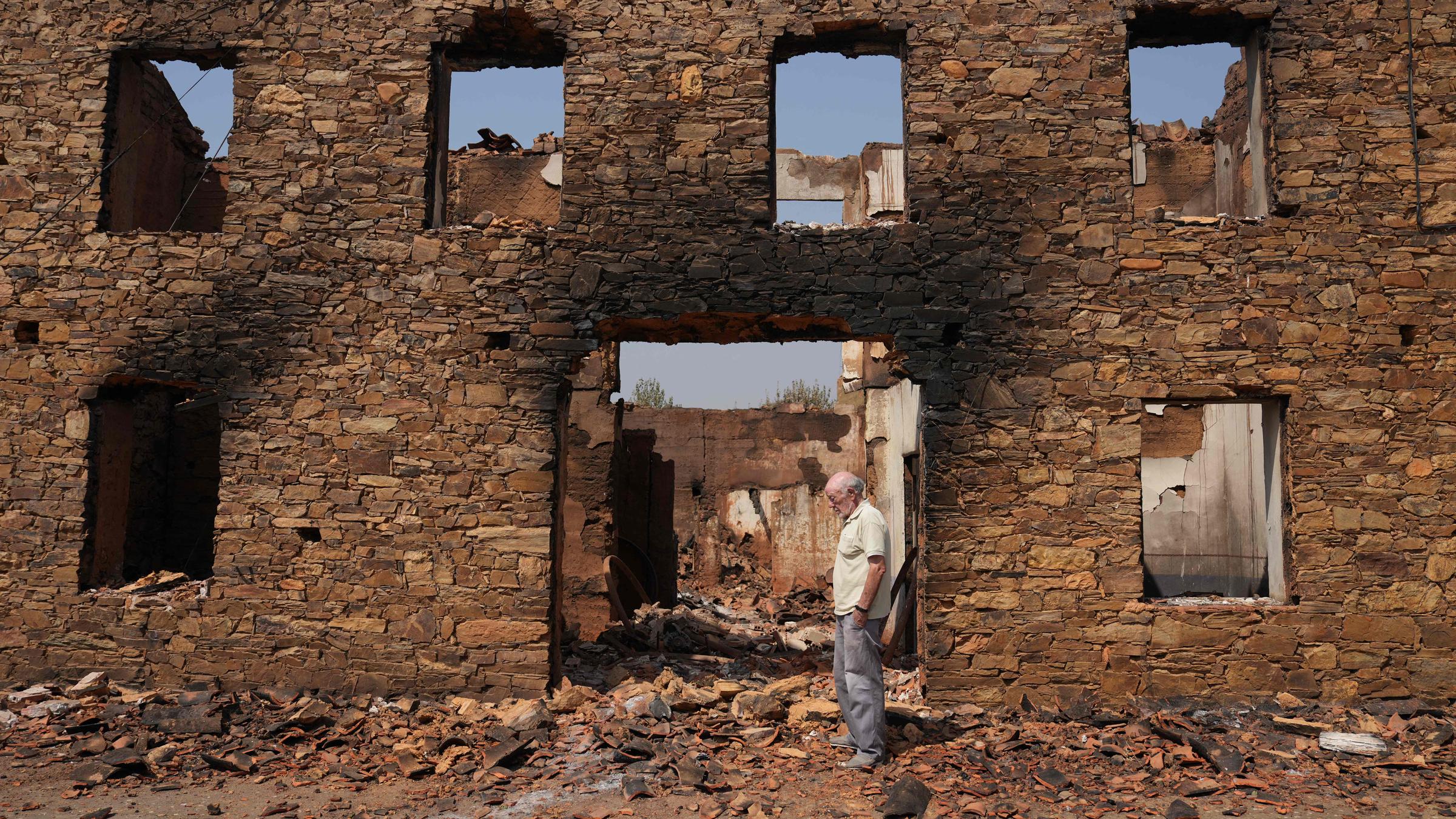 Ein Mann steht vor seinem vom Feuer zerstörten Haus.