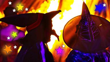 Zwei Hexen stehen nachts vor einem Feuer, man sieht nur ihre Silhouette, neben ihnen sind bunte Sterne