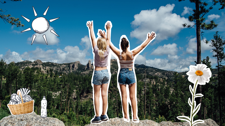 Zwei Mädchen stehen nach dem Wandern auf einem Felsen und strecken glücklich ihre Arme in die Luft