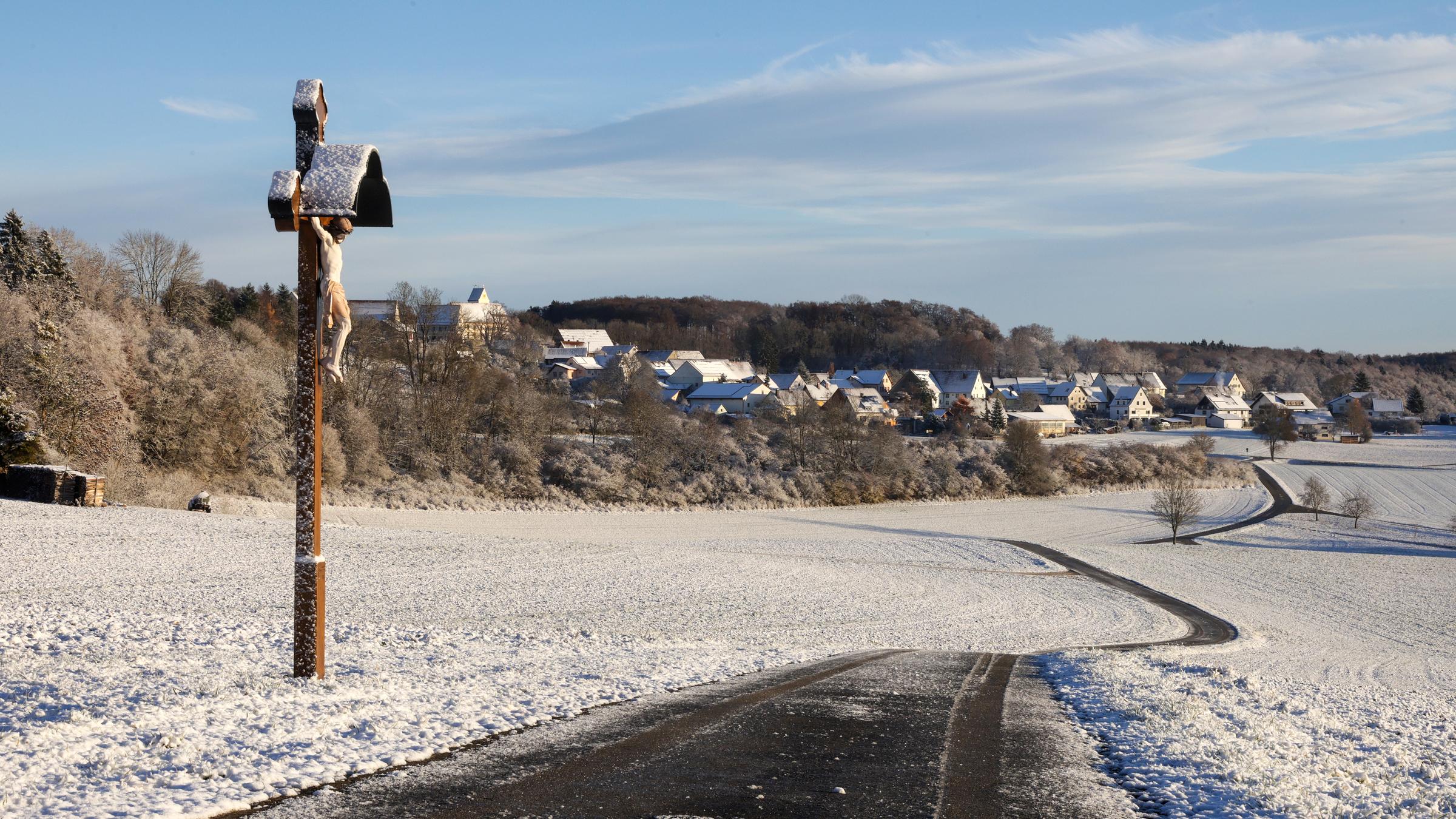 Schnee liegt am Morgen auf der Schwäbischen Alb bei Dürrenwaldstetten auf einem Weg und einem Wegkreuz.