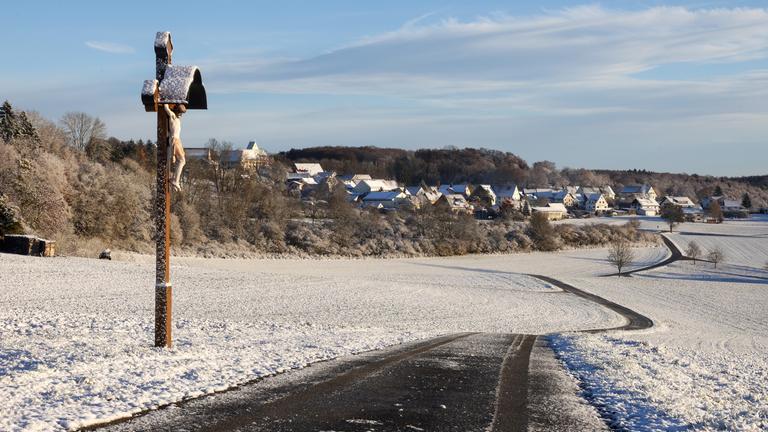 Schnee liegt am Morgen auf der Schwäbischen Alb bei Dürrenwaldstetten auf einem Weg und einem Wegkreuz.