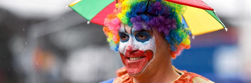 Ein Jeck mit Regenschirm im Kostüm beim Karnevalsauftakt an Weiberfastnacht in Köln
