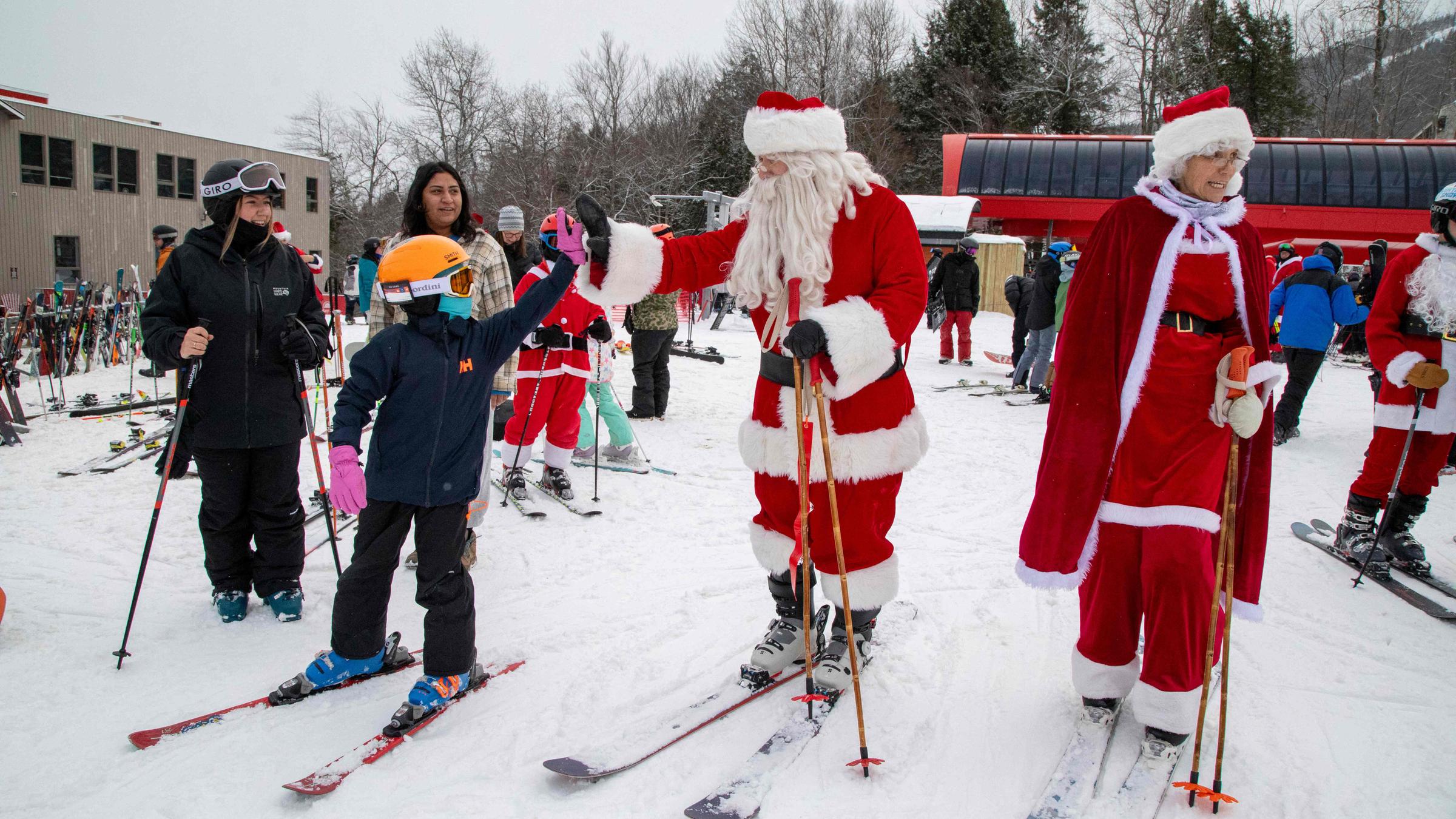 Menschen verkleidet als Weihnachtsmänner fahren Ski und Snowboard einen Hang herunter