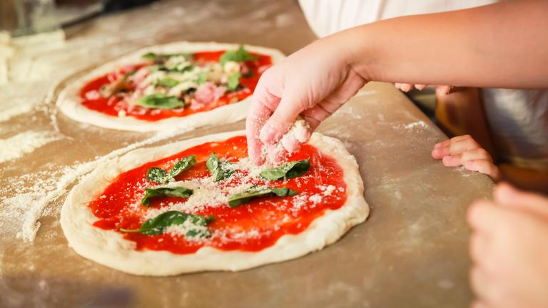 Hand streut Käse auf Pizza