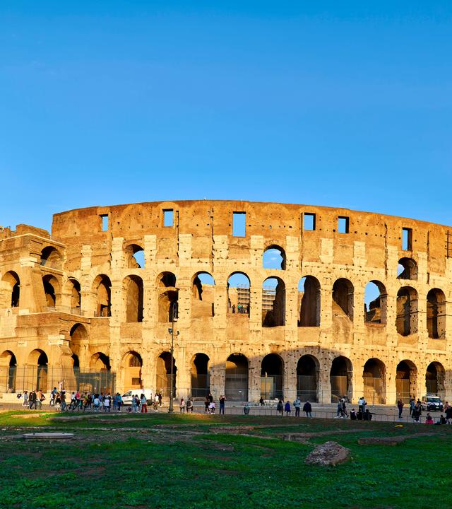Das Kolloseum vor blauem Himel. Vor dem Kolloseu laufen Menschen.