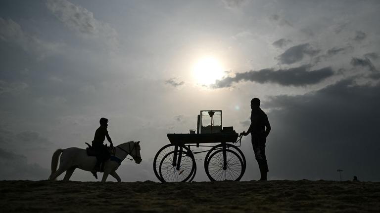 Ein Verkäufer steht mit seinem Süßigkeitenwagen am Strand.