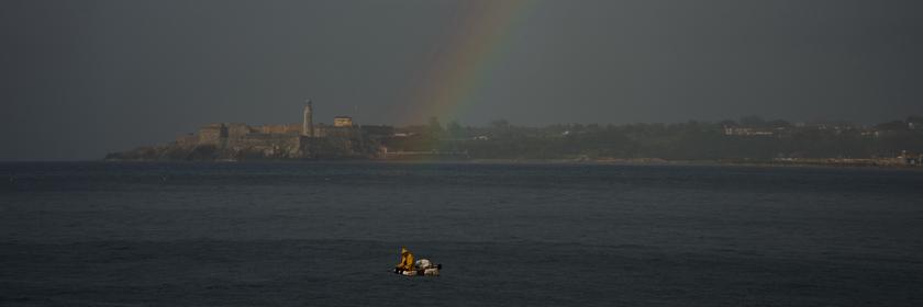 Ein Fischer fährt über das Wasser. Am Himmel erscheint ein Regenbogen. 