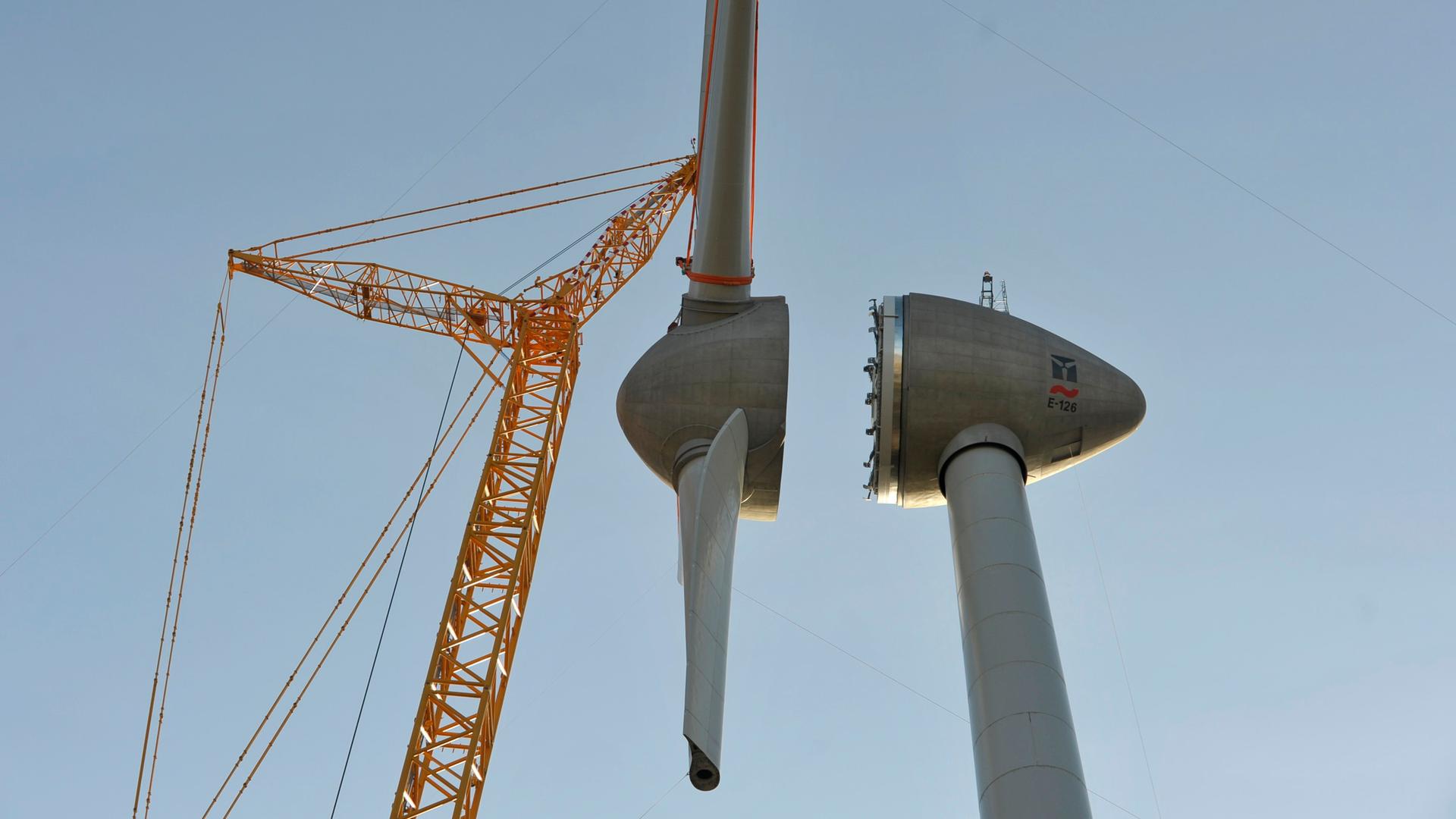 Die Rotorblätter werden mit Hilfe eines Krahns an eine Windkraftanlage gebaut
