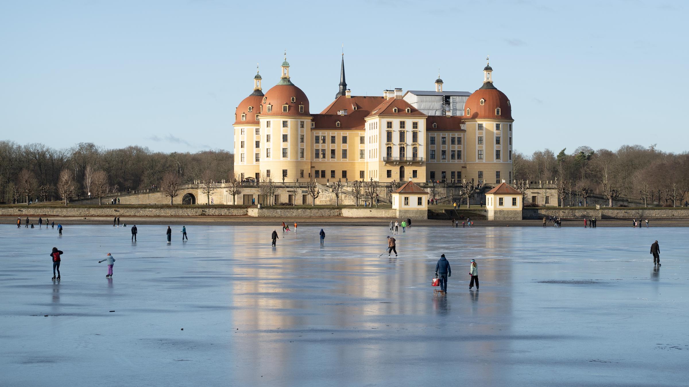 Auf dem zugefrorenen Schlossteich vor dem Schloss Moritzburg laufen Menschen Schlittschuh.