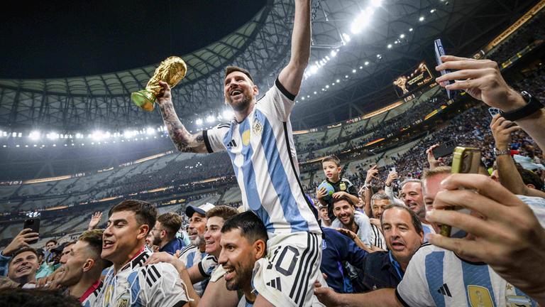 Lionel Messi hebt die WM-Trophäe hoch und wird von seinen Teamkollegen triumphierend getragen 