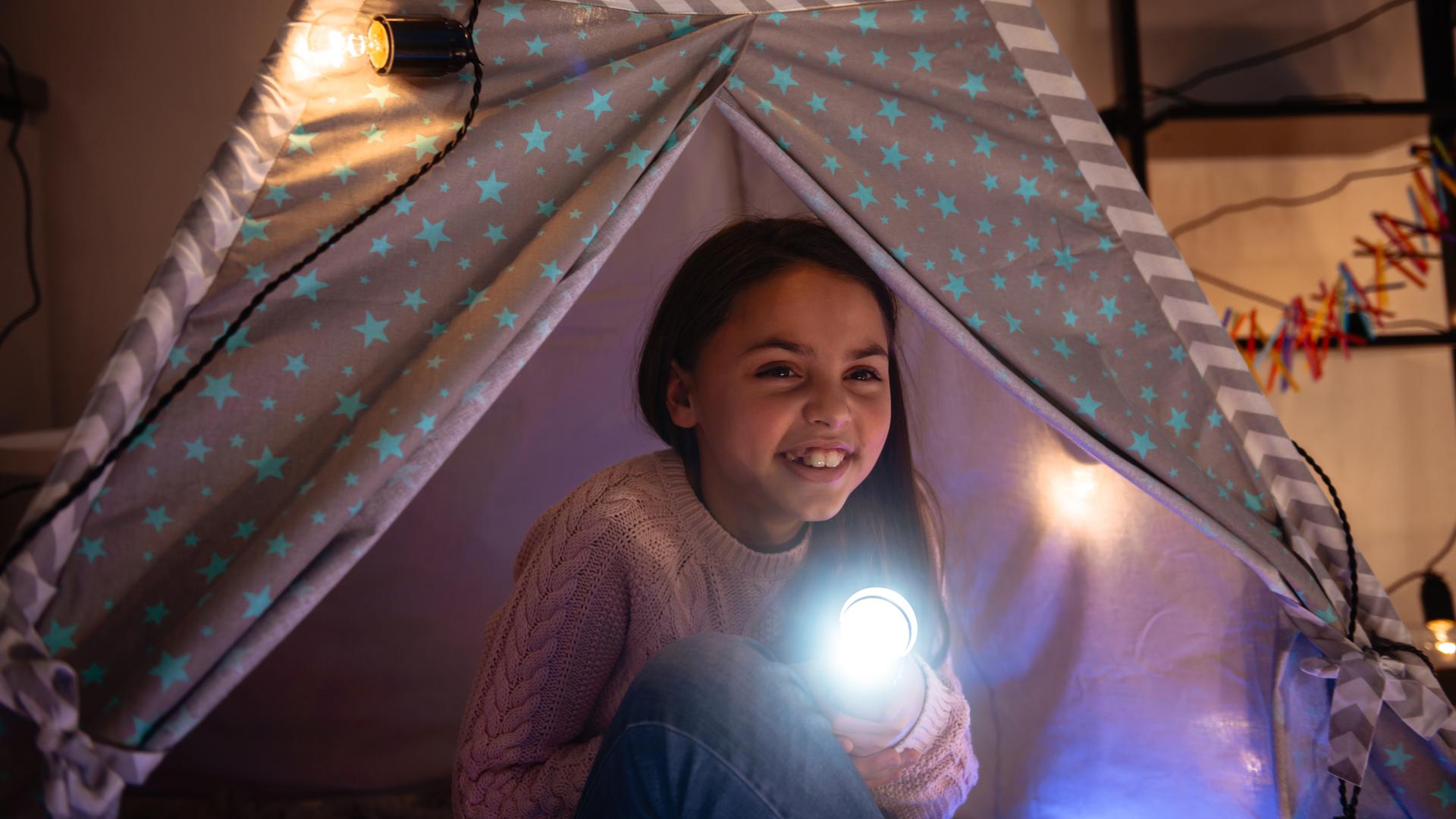 Ein Mädchen leuchtet mit einer Taschenlampe und sitzt in einem Zelt.