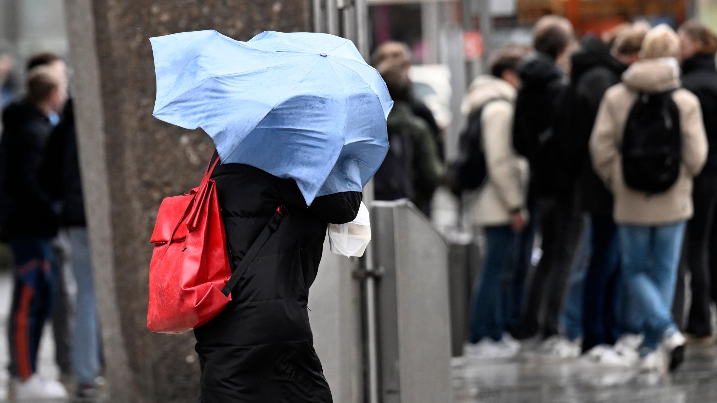 Ein Schirm fliegt einer Dame sturmbedingt um den Kopf