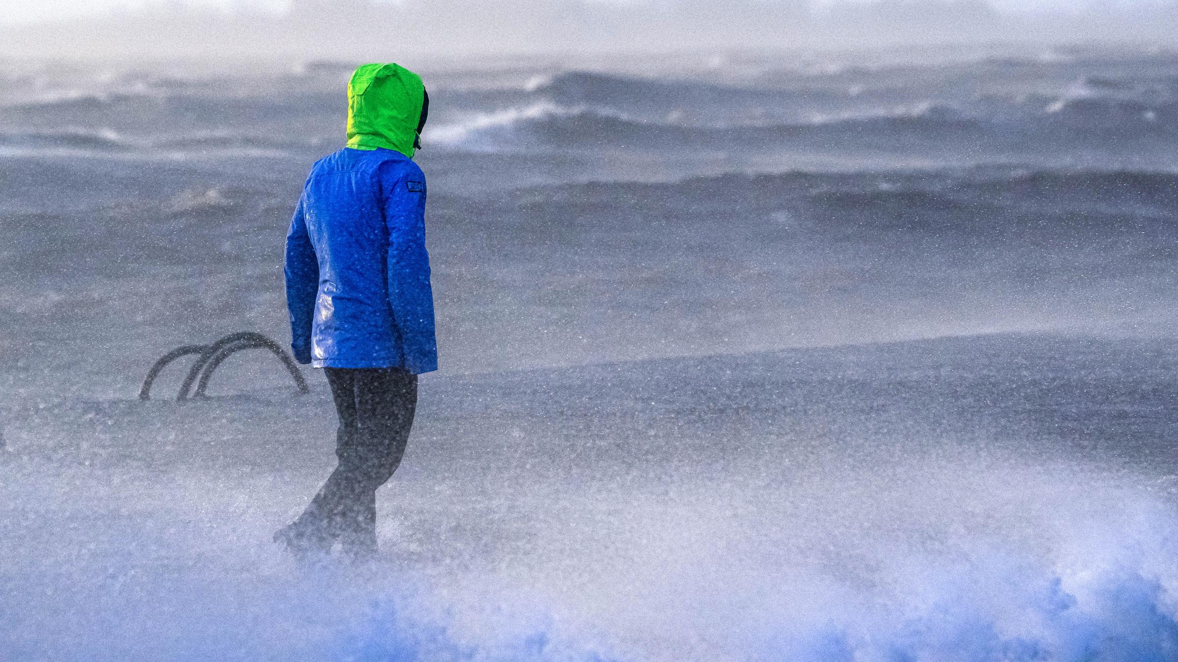 Ein Spaziergänger läuft bei Sturmflut und Wellen am Ufer der Wesermündung in Bremerhaven entlang